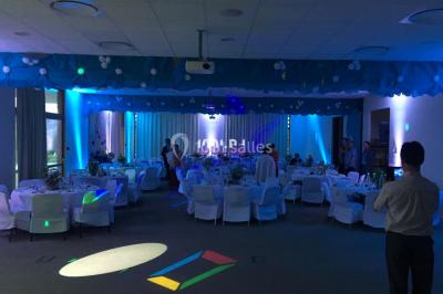 Salle de réception avec éclairage coloré, piste de danse vide et deux personnes debout près d'un bar lumineux.