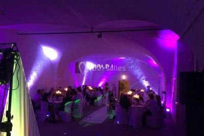 Salle de réception avec éclairage coloré, piste de danse vide et deux personnes debout près d'un bar lumineux.