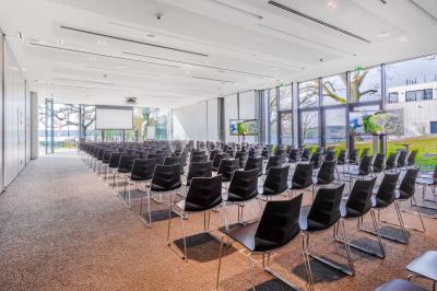 Miniature Location salle Froidchapelle (Hainaut) - Golden Lakes Hôtel #3 Terrasse en bois avec table et chaises, vue sur un jardin verdoyant et un lac au coucher du soleil.