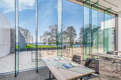 Miniature Location salle Froidchapelle (Hainaut) - Golden Lakes Hôtel #9 Terrasse en bois avec table et chaises, vue sur un jardin verdoyant et un lac au coucher du soleil.