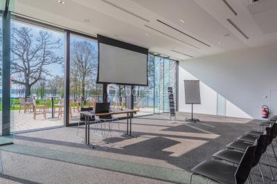 Miniature Location salle Froidchapelle (Hainaut) - Golden Lakes Hôtel #17 Terrasse en bois avec table et chaises, vue sur un jardin verdoyant et un lac au coucher du soleil.