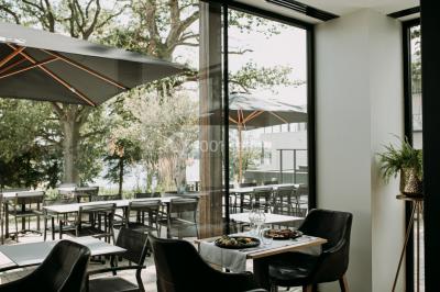 Miniature Location salle Froidchapelle (Hainaut) - Golden Lakes Hôtel #19 Terrasse en bois avec table et chaises, vue sur un jardin verdoyant et un lac au coucher du soleil.