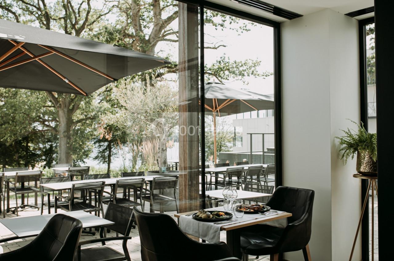 Salle de restaurant lumineuse avec vue sur une terrasse extérieure équipée de tables, chaises et parasols.