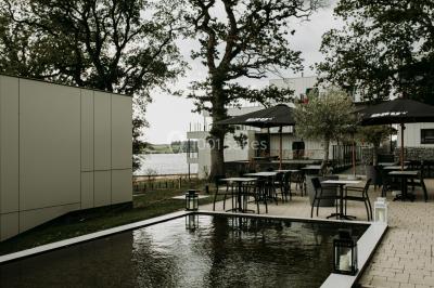 Miniature Location salle Froidchapelle (Hainaut) - Golden Lakes Hôtel #21 Terrasse en bois avec table et chaises, vue sur un jardin verdoyant et un lac au coucher du soleil.