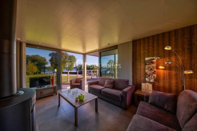 Miniature Location salle Froidchapelle (Hainaut) - Golden Lakes Hôtel #25 Terrasse en bois avec table et chaises, vue sur un jardin verdoyant et un lac au coucher du soleil.