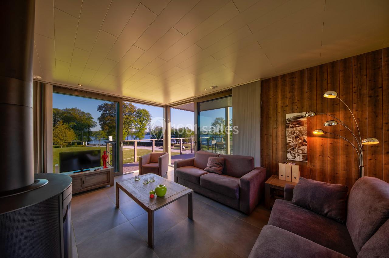 Salon lumineux avec canapés, table basse, lampadaire et grande baie vitrée donnant sur un paysage verdoyant.