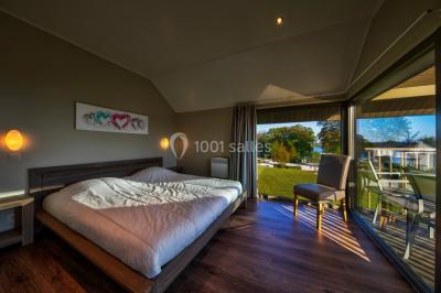 Miniature Location salle Froidchapelle (Hainaut) - Golden Lakes Hôtel #26 Terrasse en bois avec table et chaises, vue sur un jardin verdoyant et un lac au coucher du soleil.