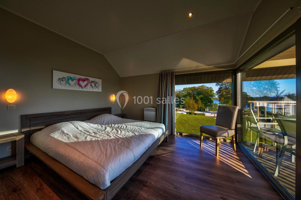 Chambre lumineuse avec lit double, grandes baies vitrées donnant sur un jardin et un paysage extérieur.