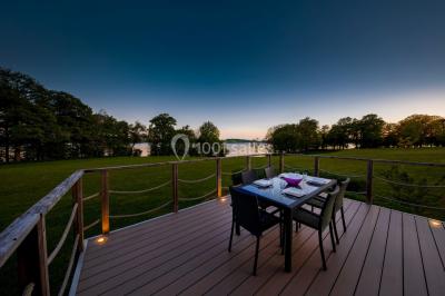 Miniature Location salle Froidchapelle (Hainaut) - Golden Lakes Hôtel #27 Terrasse en bois avec table et chaises, vue sur un jardin verdoyant et un lac au coucher du soleil.