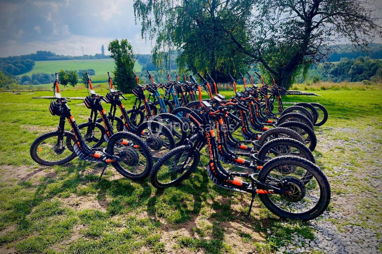 Rangée de trottinettes tout-terrain alignées sur une pelouse, avec un paysage vallonné en arrière-plan.