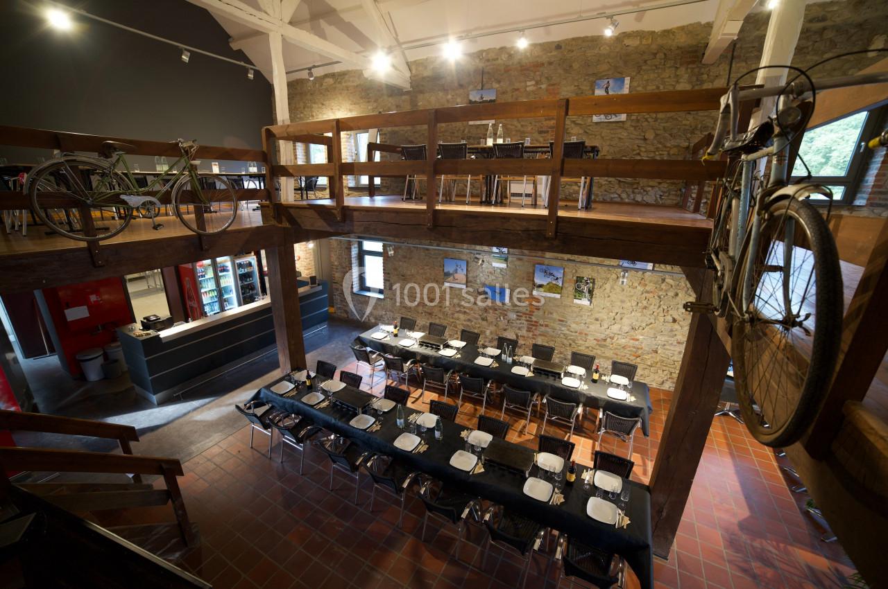 Salle à manger spacieuse avec tables dressées, murs en pierre, mezzanine en bois et vélos accrochés en décoration.