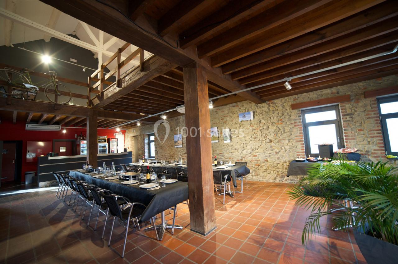 Salle de réception avec tables dressées, murs en pierre, poutres apparentes et éclairage naturel.