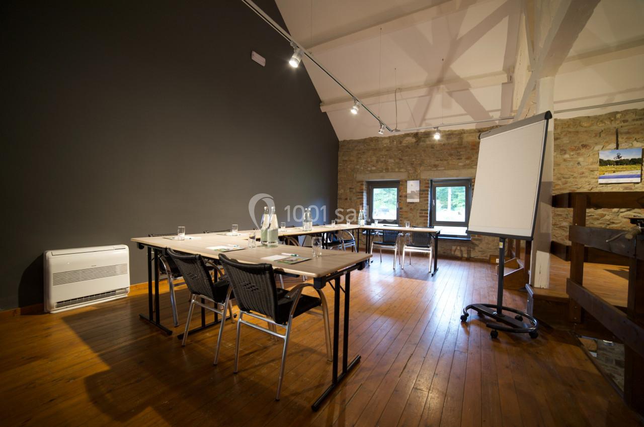 Salle de réunion lumineuse avec tables, chaises, paperboard, bouteilles d'eau et murs en briques apparentes.
