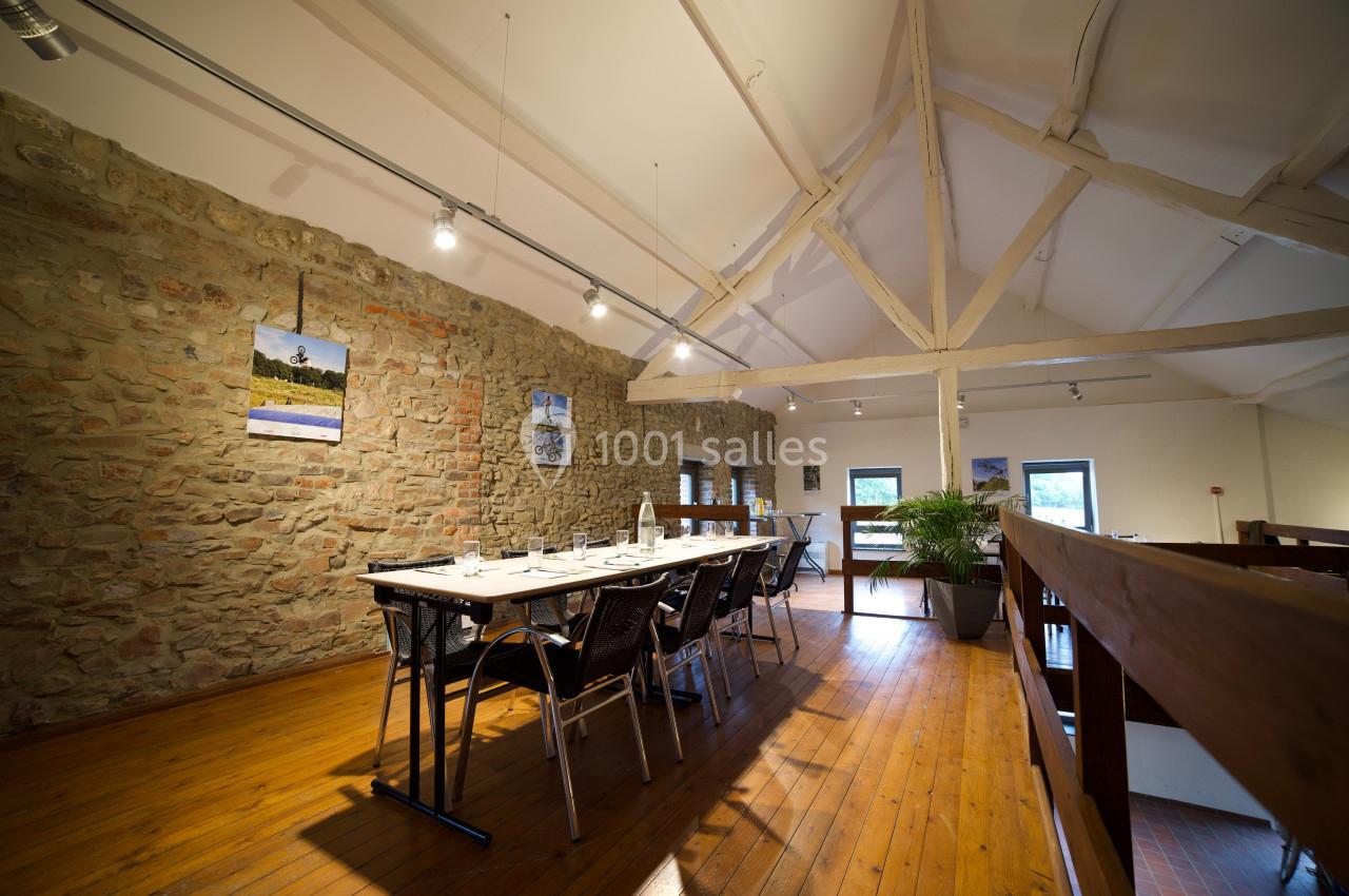 Salle à manger lumineuse avec table dressée, murs en pierre apparente, poutres blanches et parquet en bois.