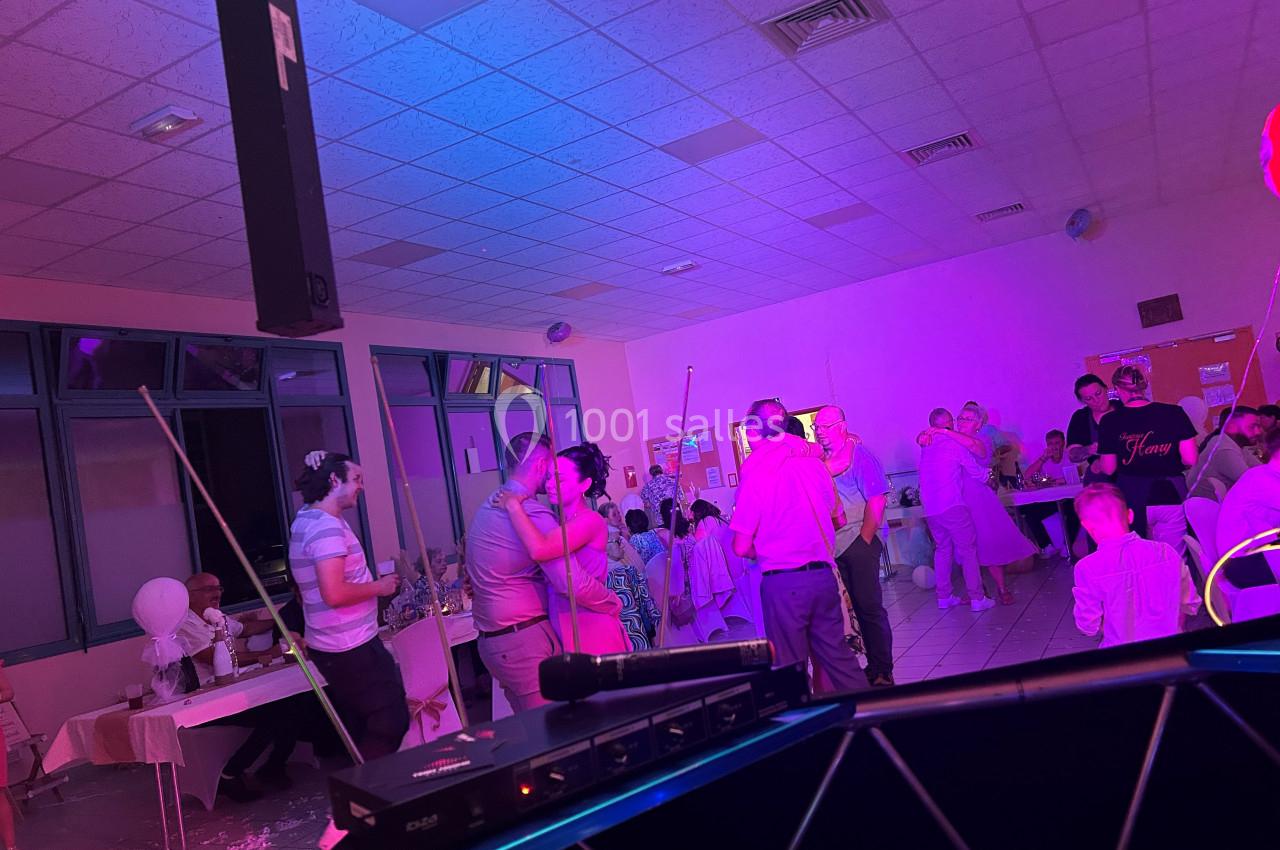 Des personnes dansent et discutent dans une salle éclairée par des lumières colorées lors d'un événement festif.