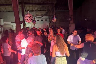 Miniature DJ Geville (Meuse) - Team MooMa Events #9 Des personnes dansent dans une salle éclairée par des lumières rouges, entourées de tables dressées pour un événement.