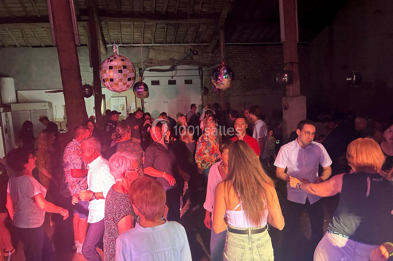 Des personnes dansent et discutent dans une salle éclairée par des lumières colorées et des boules à facettes.