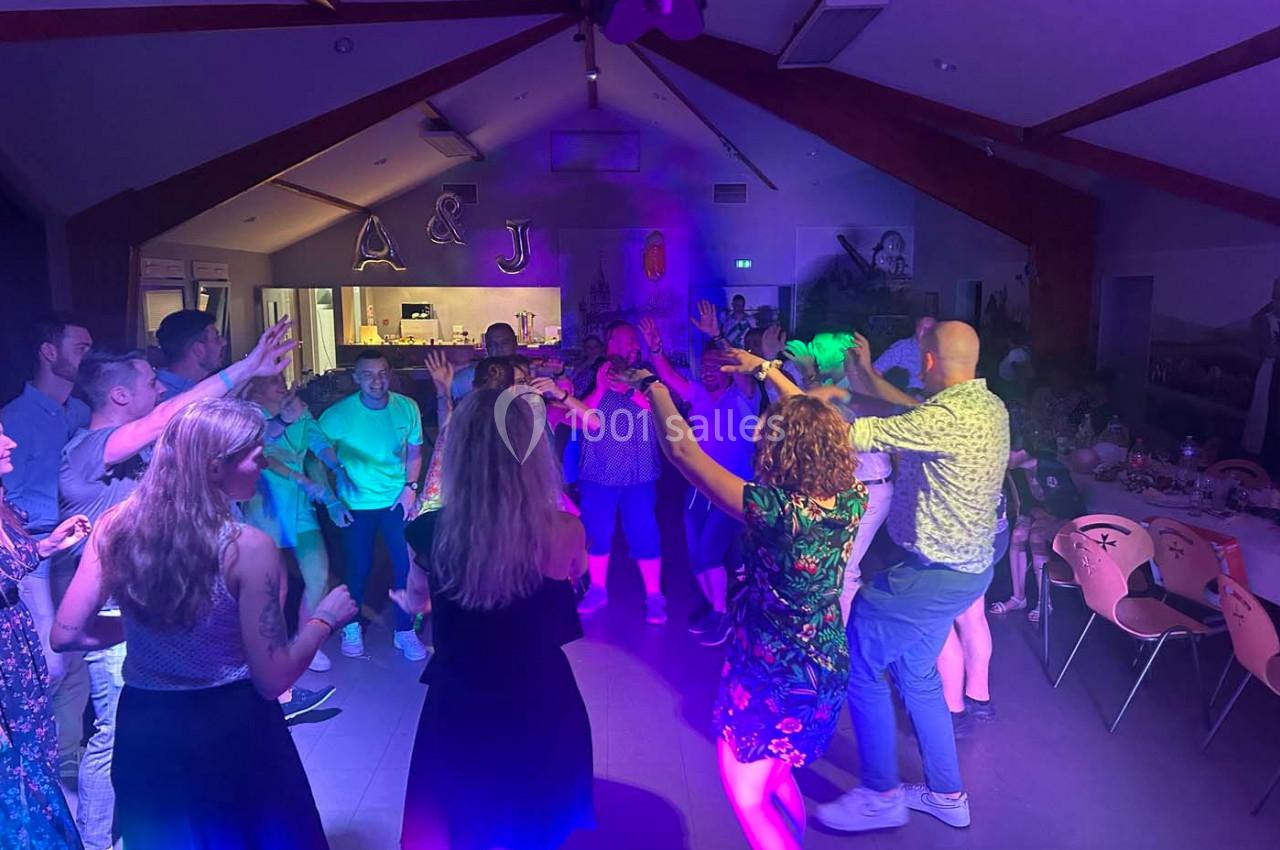 Des personnes dansent dans une salle éclairée par des lumières colorées, avec des décorations en arrière-plan.