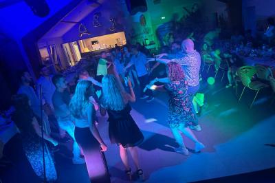 Miniature DJ Geville (Meuse) - Team MooMa Events #18 Des personnes dansent dans une salle éclairée par des lumières rouges, entourées de tables dressées pour un événement.