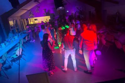 Miniature DJ Geville (Meuse) - Team MooMa Events #12 Des personnes dansent dans une salle éclairée par des lumières rouges, entourées de tables dressées pour un événement.