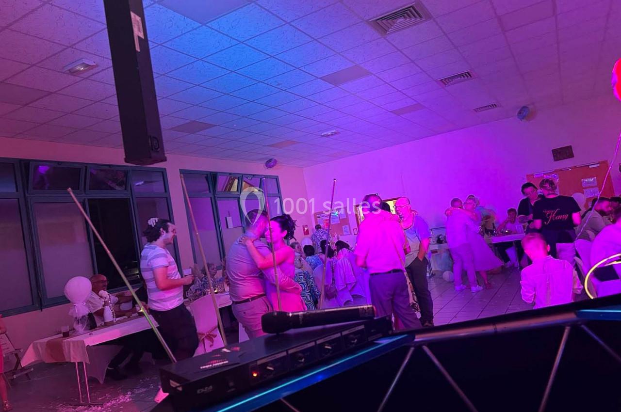 Des personnes dansent et discutent dans une salle éclairée par des lumières colorées, lors d'un événement festif.