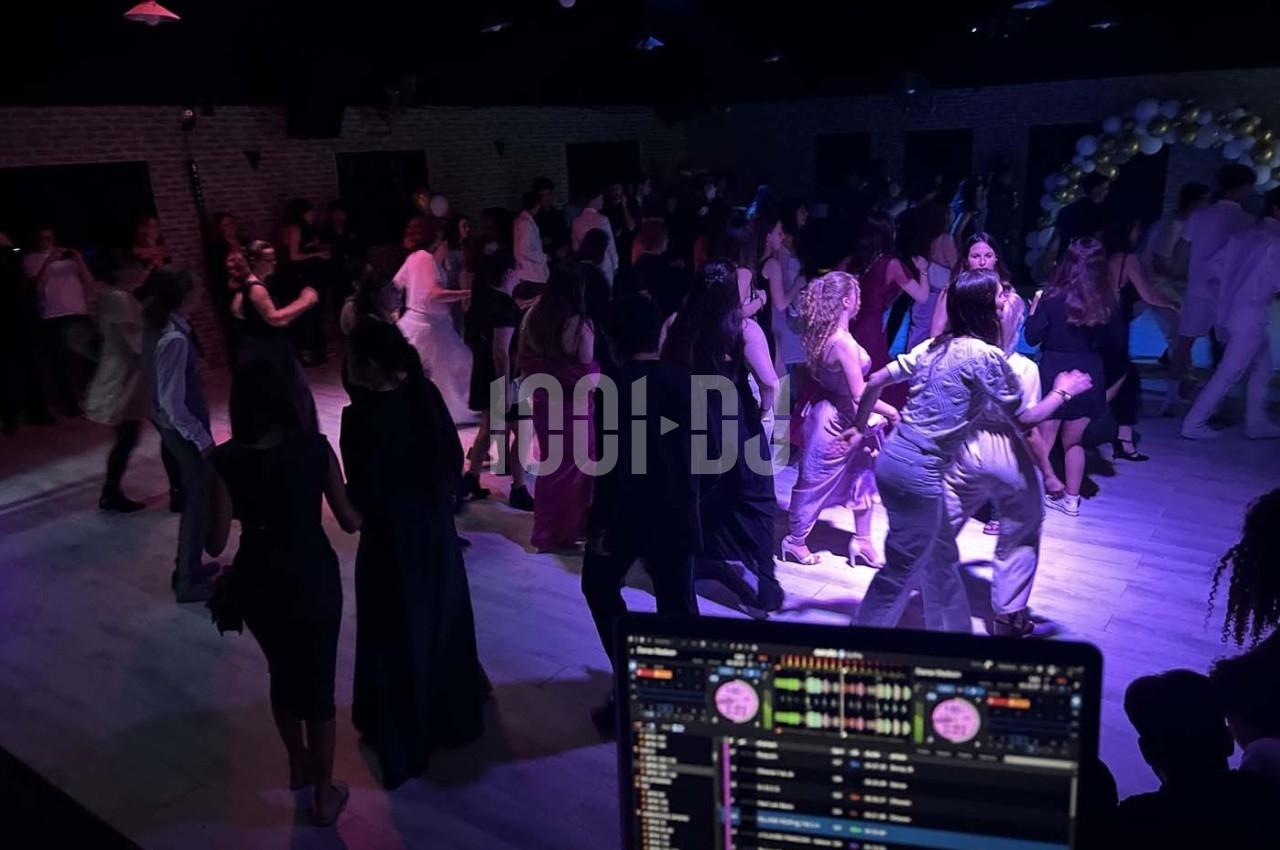 Groupe de personnes dansant dans une salle sombre avec un écran de mixage de DJ visible au premier plan.