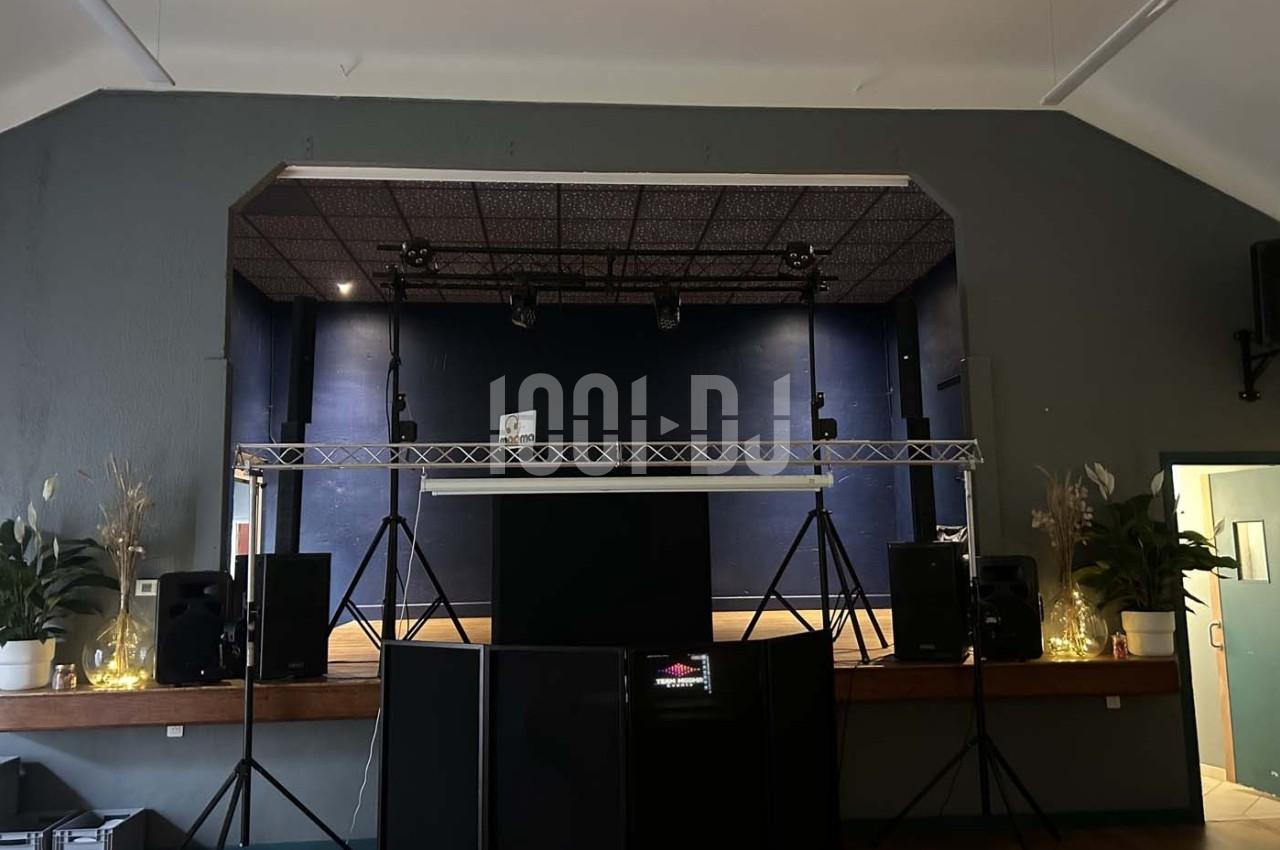 Scène intérieure avec éclairage tamisé, équipement audio et décoration végétale sur les côtés.