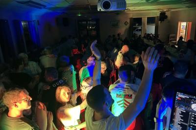 Miniature DJ Geville (Meuse) - Team MooMa Events #34 Des personnes dansent dans une salle éclairée par des lumières rouges, entourées de tables dressées pour un événement.