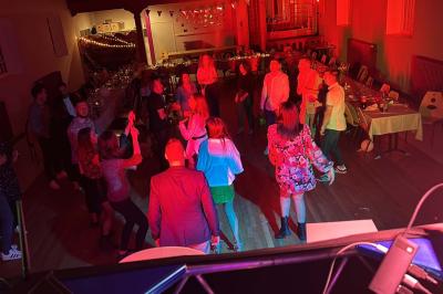 Miniature DJ Geville (Meuse) - Team MooMa Events #37 Des personnes dansent dans une salle éclairée par des lumières rouges, entourées de tables dressées pour un événement.