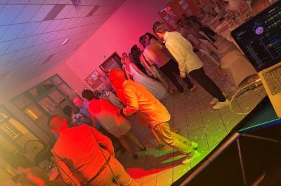 Miniature DJ Geville (Meuse) - Team MooMa Events #8 Des personnes dansent dans une salle éclairée par des lumières rouges, entourées de tables dressées pour un événement.