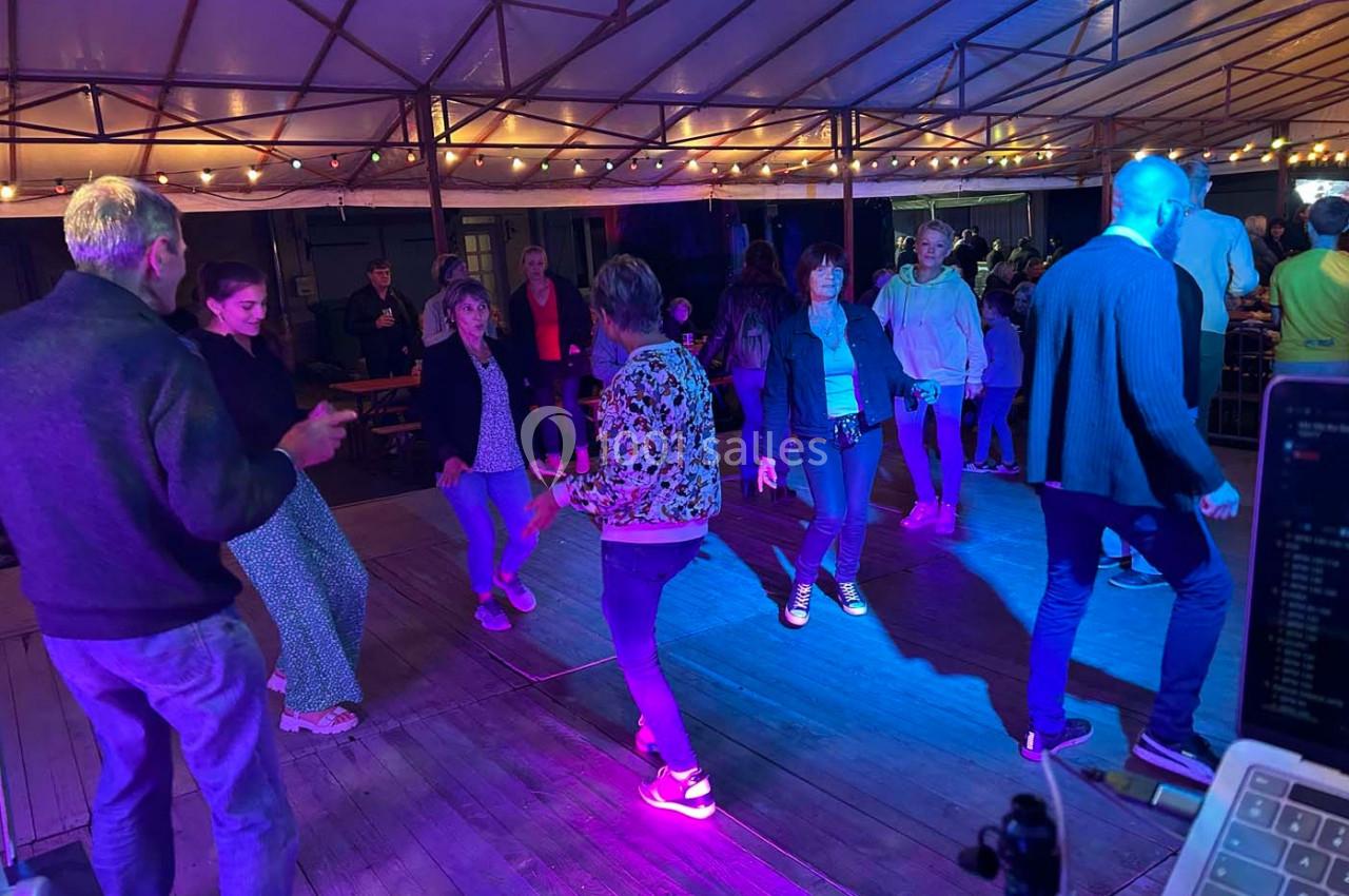 Des personnes dansent sous une structure éclairée par des guirlandes lumineuses, dans une ambiance conviviale en soirée.
