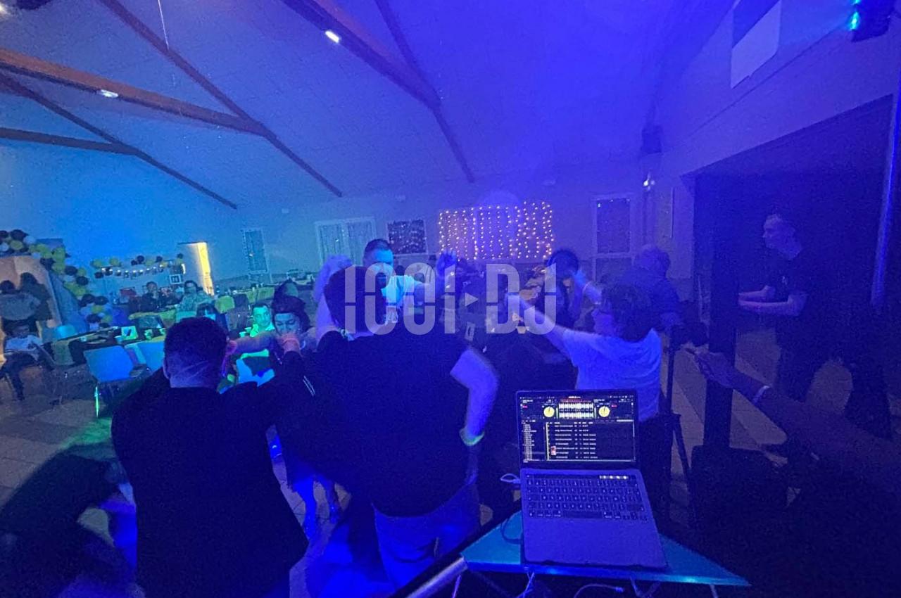 Groupe de personnes dans une salle éclairée par des lumières colorées, dansant près d'une table de mixage.