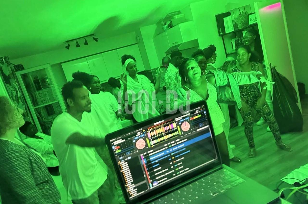 Des personnes dansent et s'amusent dans une pièce éclairée par une lumière verte, avec un ordinateur en premier plan.