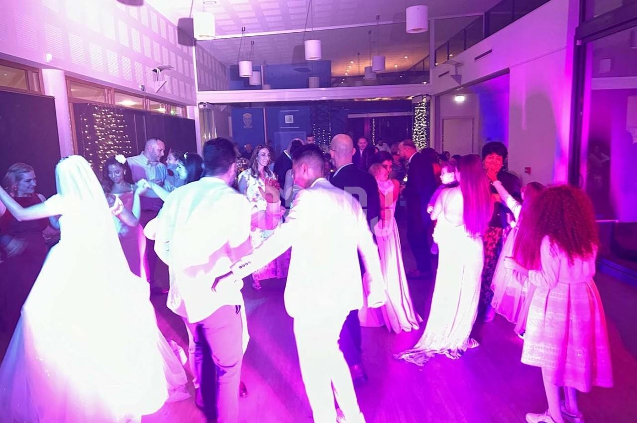 Des invités dansent dans une salle éclairée de lumières colorées, lors d'une fête ou d'une célébration.