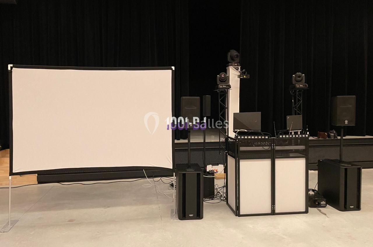 Équipement de sonorisation et projection installé dans une salle avec écran, enceintes et matériel DJ.