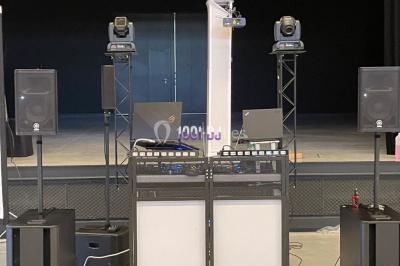 Équipement de sonorisation comprenant enceintes, projecteurs et consoles, installé sur une scène vide.
