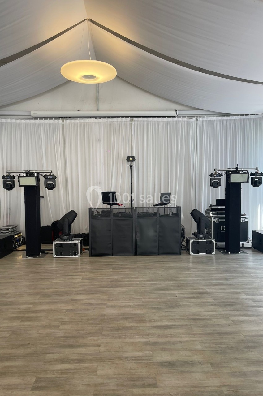 Équipement de sonorisation et éclairage installé dans une salle avec sol en bois et rideaux blancs.