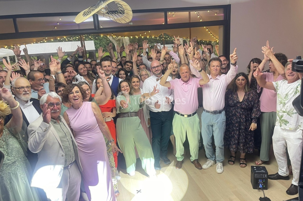 Un groupe de personnes souriantes pose ensemble dans une salle décorée, levant les bras dans une ambiance festive.