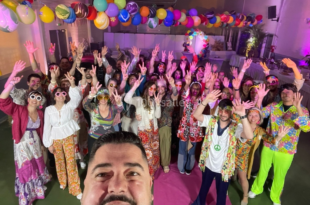 Un groupe de personnes en tenue colorée lève les bras dans une salle décorée de ballons lors d'un événement festif.
