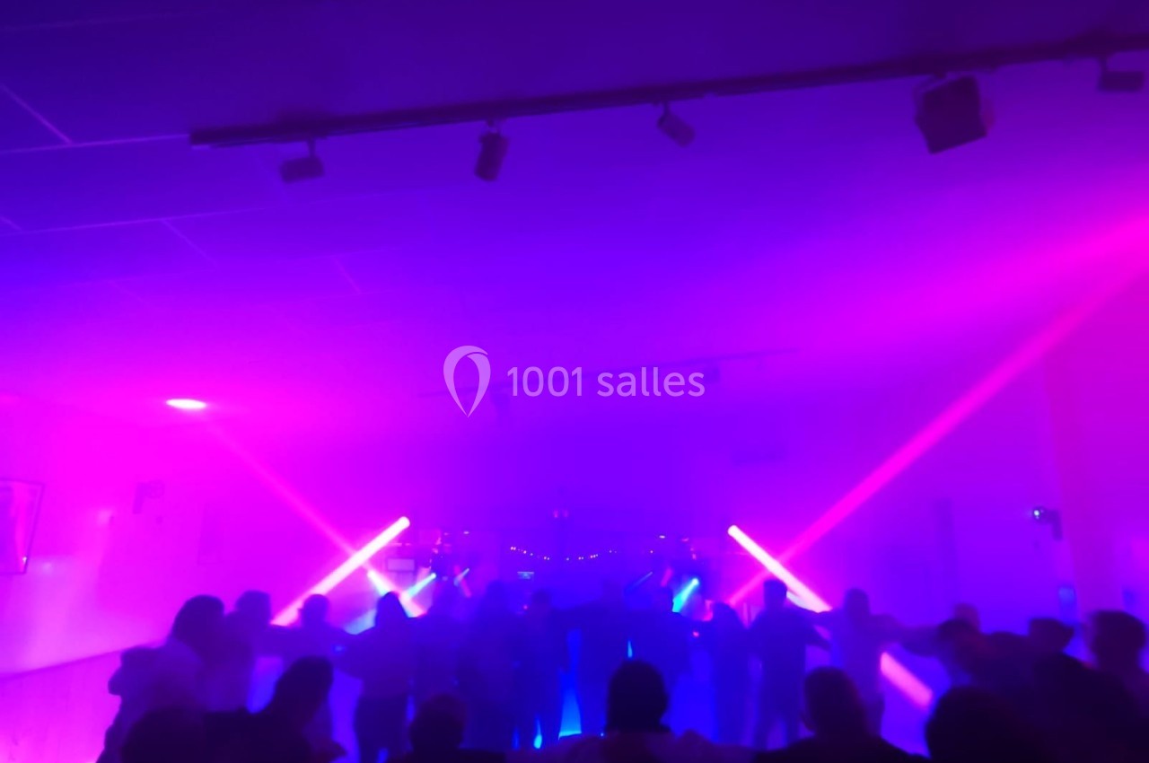 Des silhouettes de personnes dansant sous des lumières violettes et roses dans une ambiance festive et enfumée.