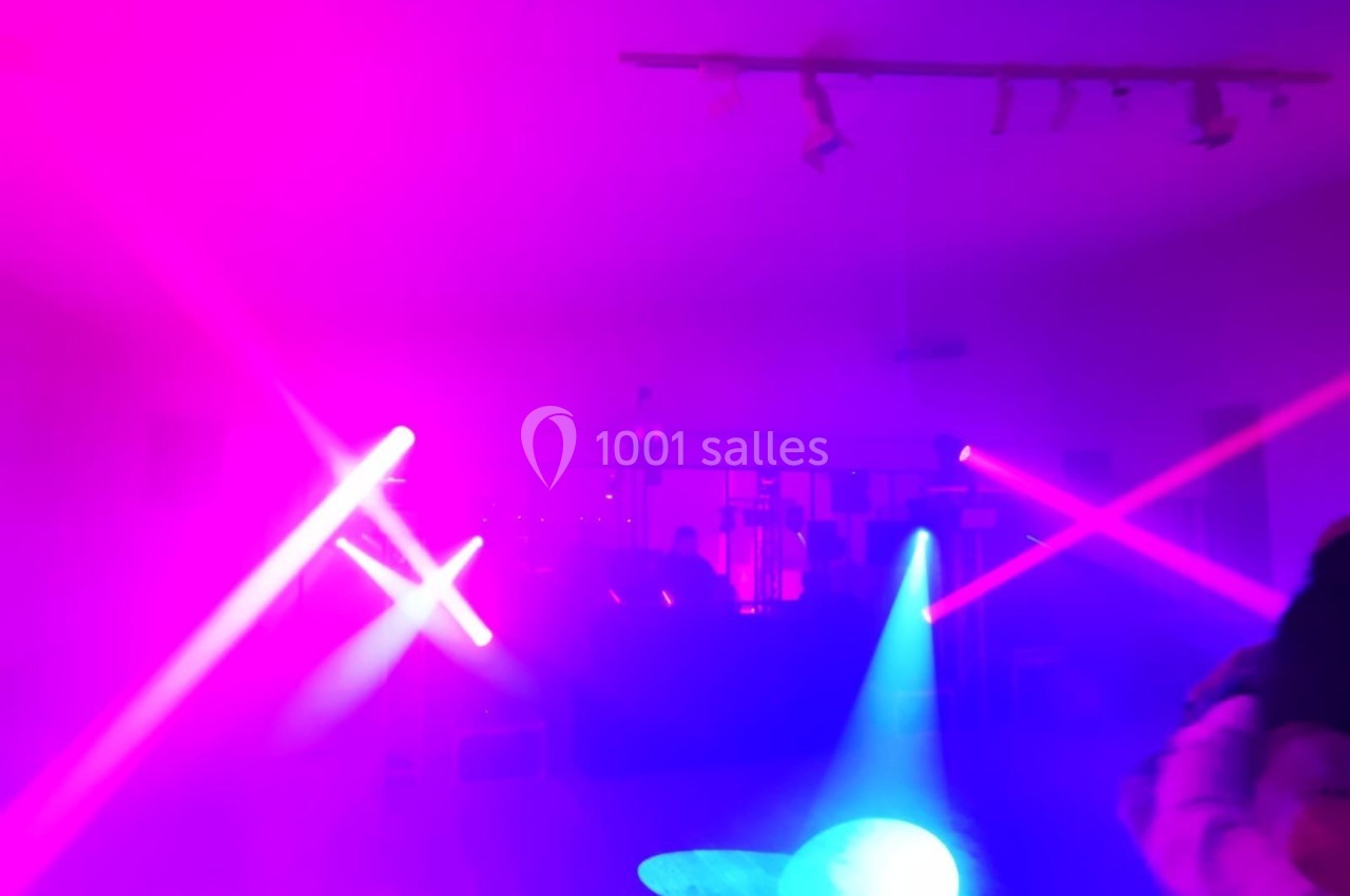 Salle sombre éclairée par des lumières colorées violettes et bleues, avec des projecteurs et une ambiance festive.