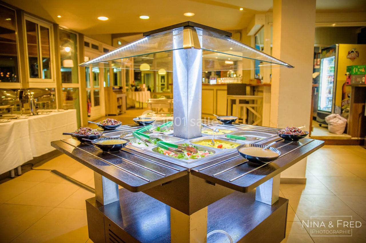 Buffet lumineux avec compartiments remplis de salades et condiments, entouré de bols dans une salle de restaurant.