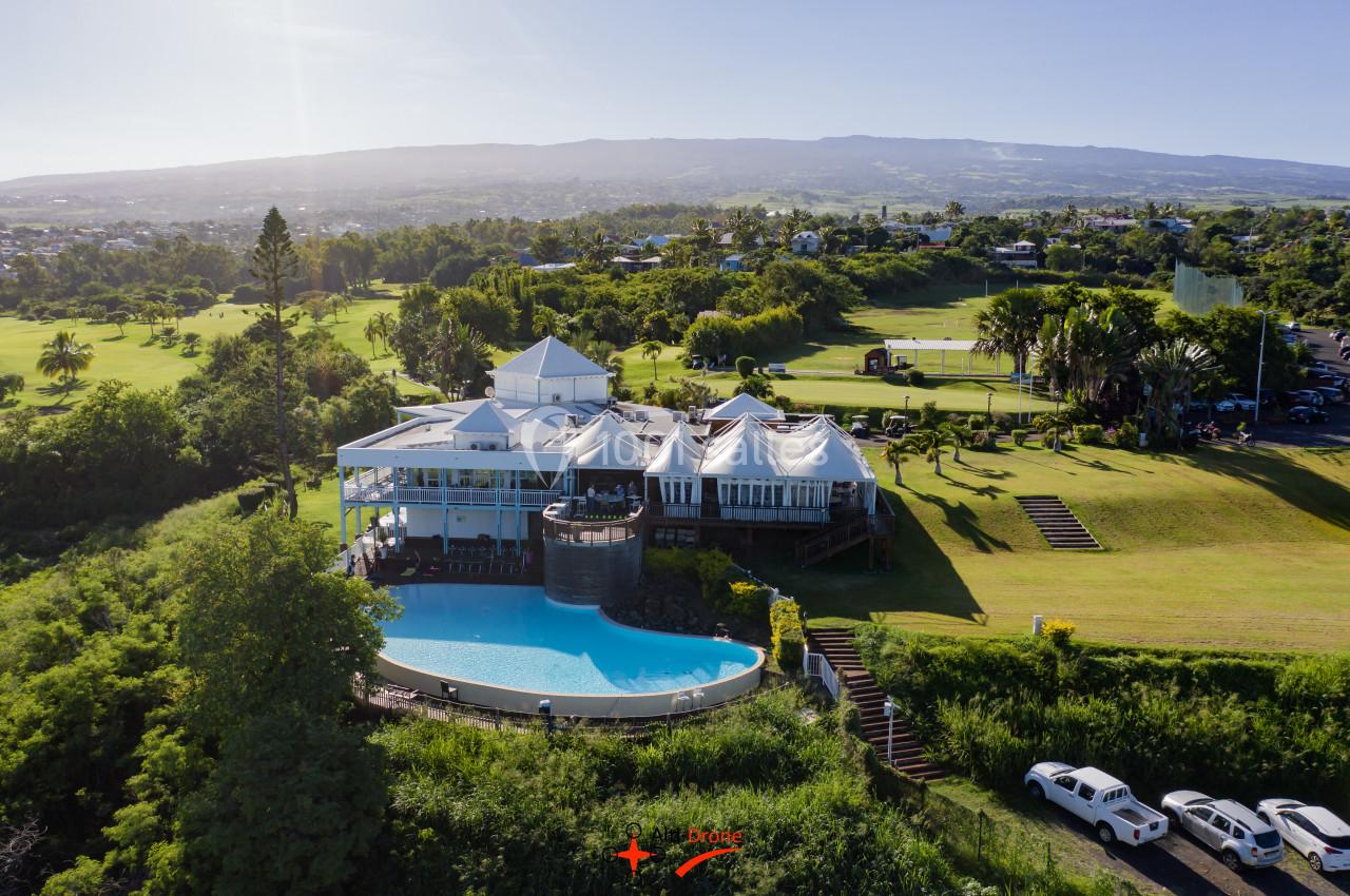 Vue aérienne d'un bâtiment avec piscine à débordement, entouré de verdure et d'un paysage vallonné.