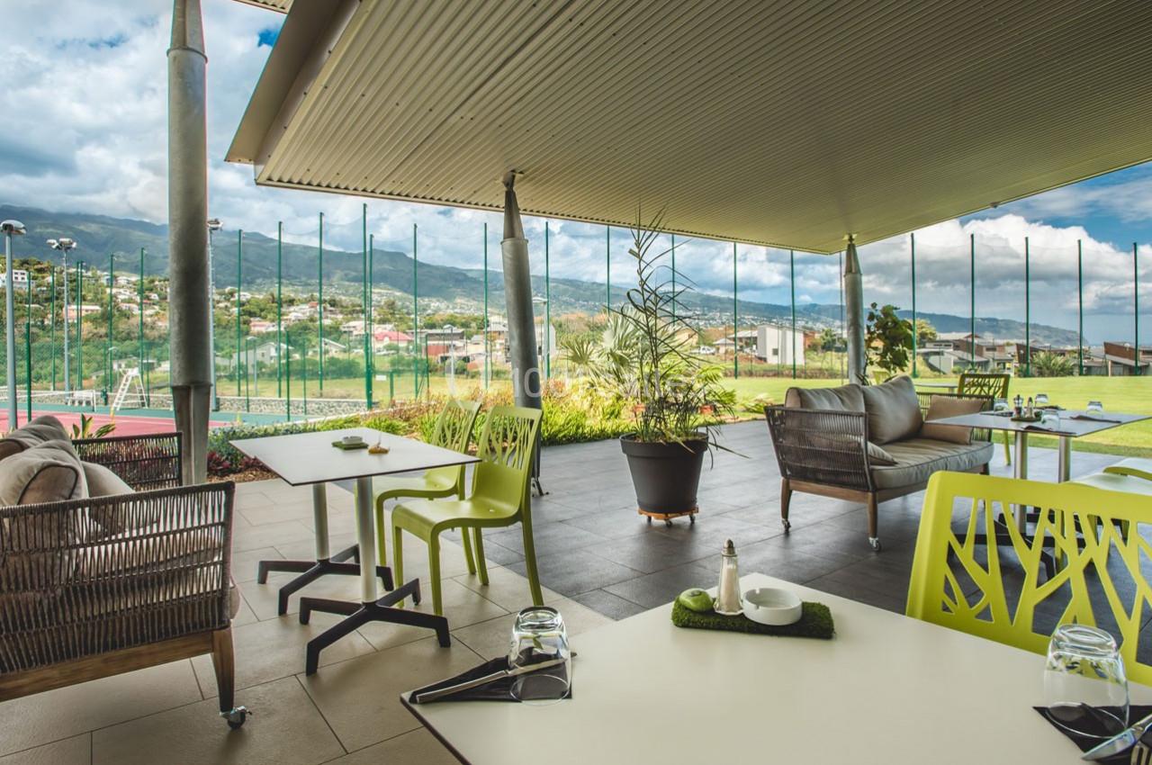 Terrasse couverte avec mobilier moderne, vue sur un jardin verdoyant et des collines en arrière-plan.