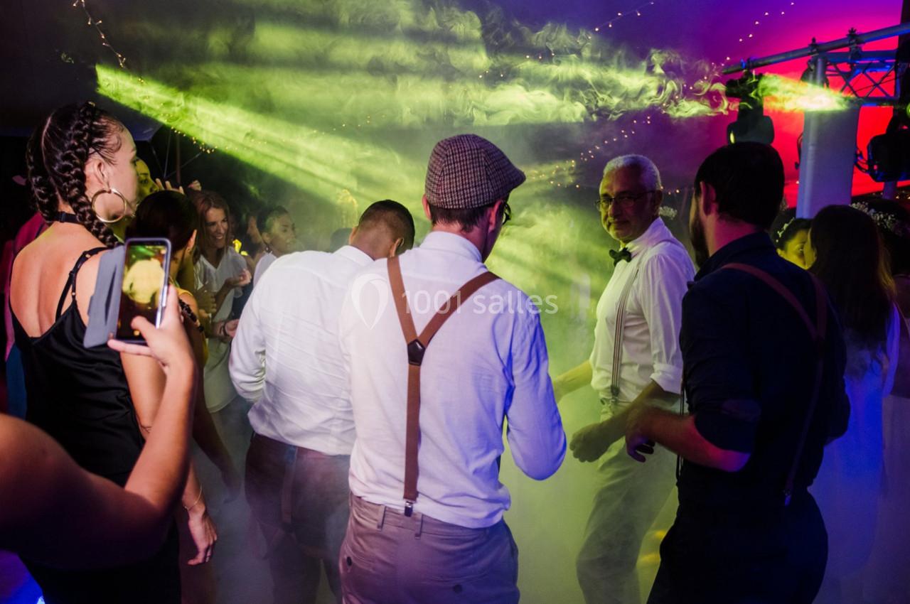Des personnes dansent sous des lumières colorées et des effets de fumée lors d'une soirée festive.