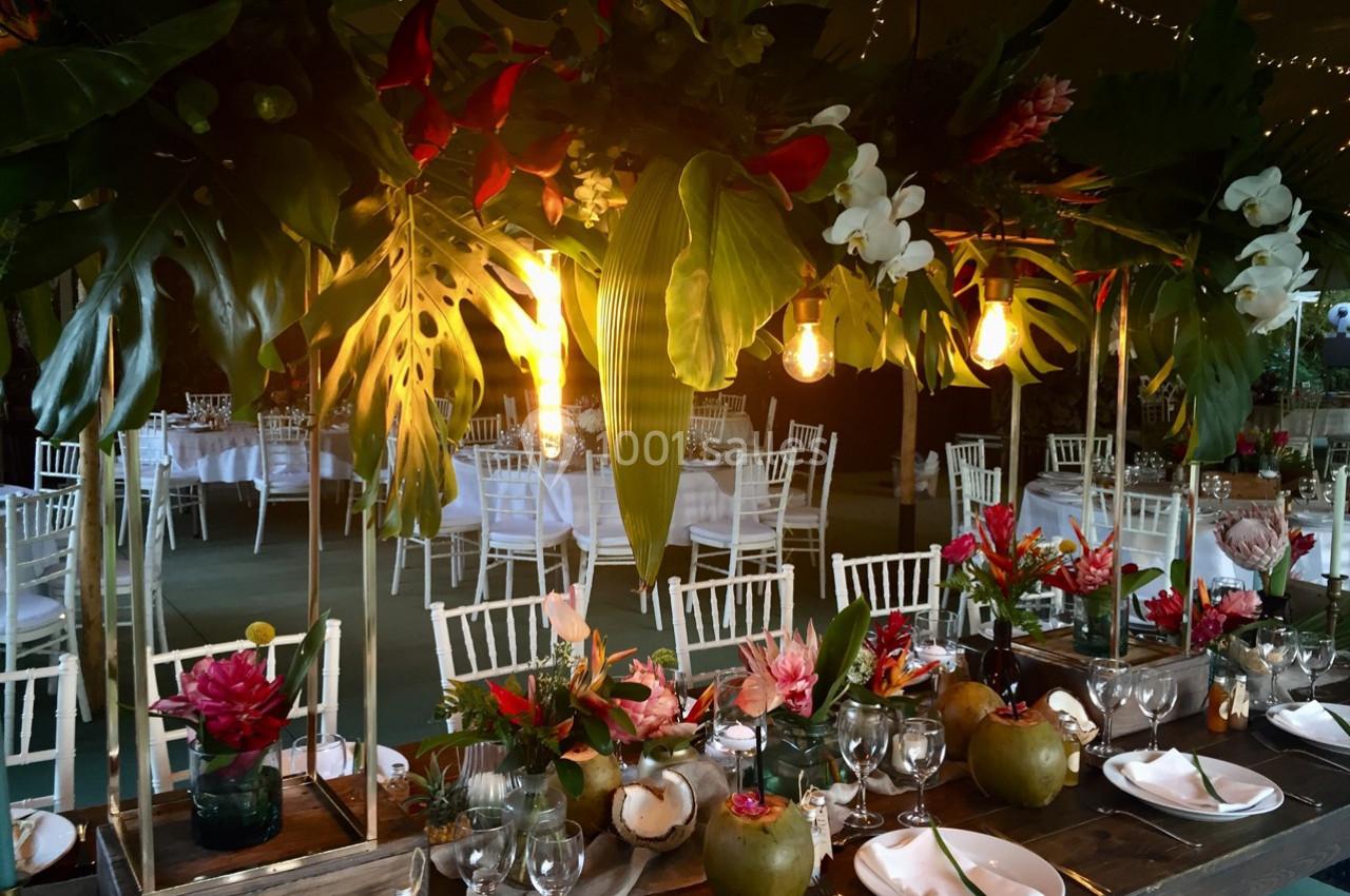 Table décorée avec des fleurs tropicales, des feuilles luxuriantes et des noix de coco, dans une salle éclairée par des…