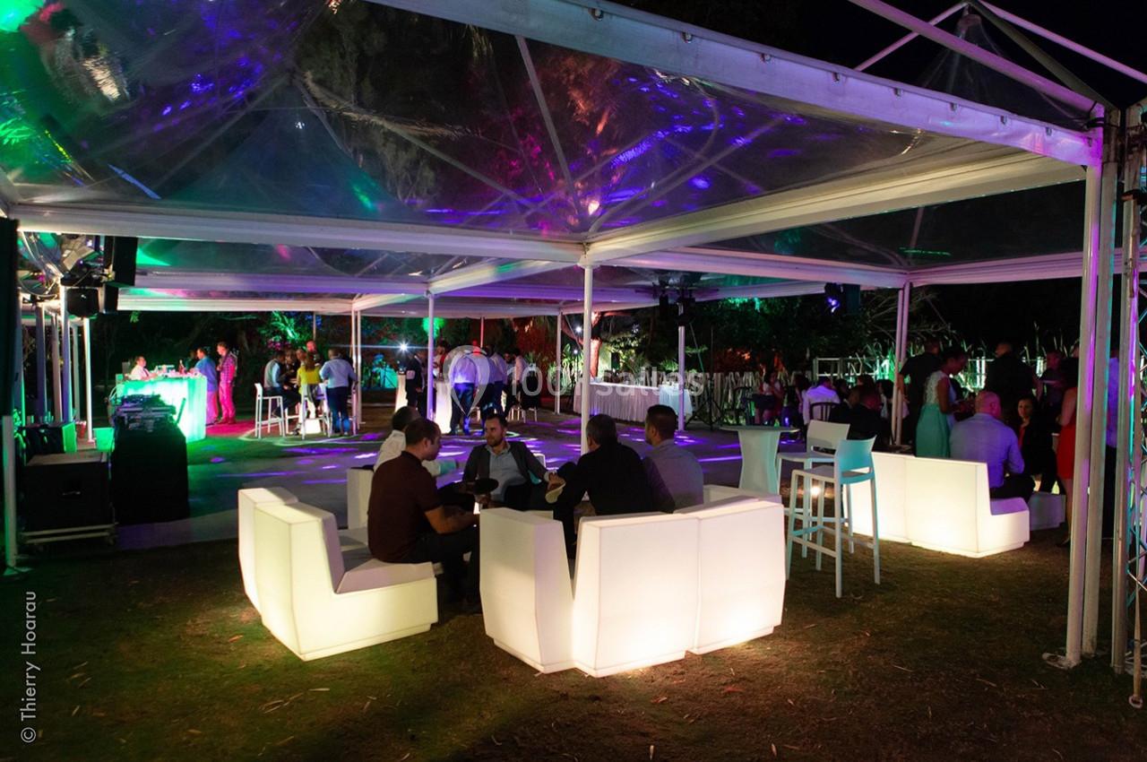 Soirée en extérieur sous des tentes transparentes, avec éclairages colorés, tables hautes et fauteuils lumineux.