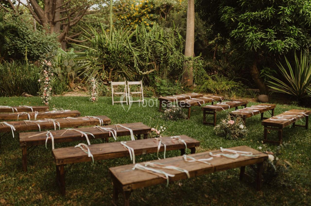 Bancs en bois disposés sur une pelouse pour une cérémonie en plein air, entourés de végétation et de fleurs.