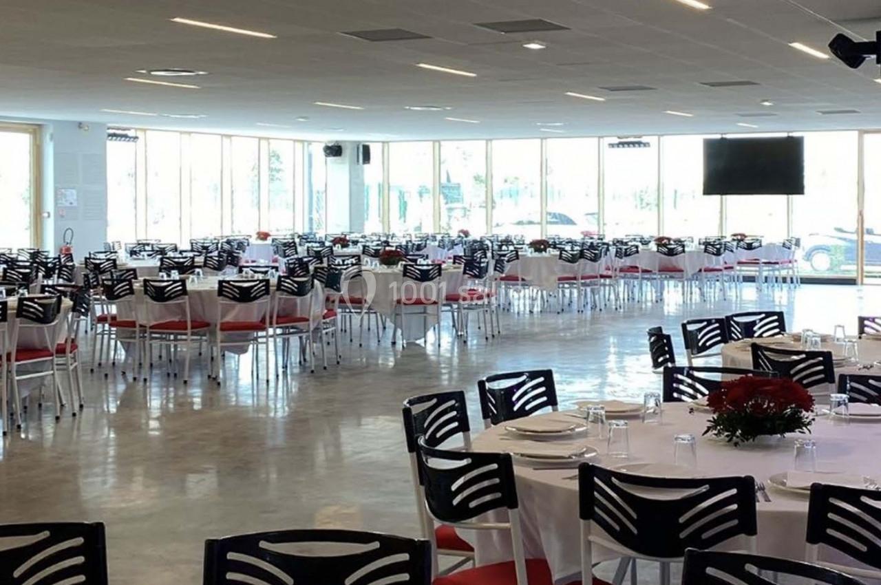 Salle de réception lumineuse avec des tables dressées, nappes blanches et chaises noires, prête pour un événement.