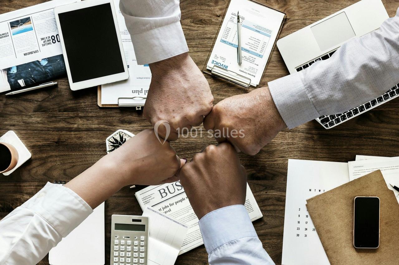 Quatre personnes se serrant les poings au-dessus d'un bureau avec des documents, un ordinateur portable et une calculatrice.